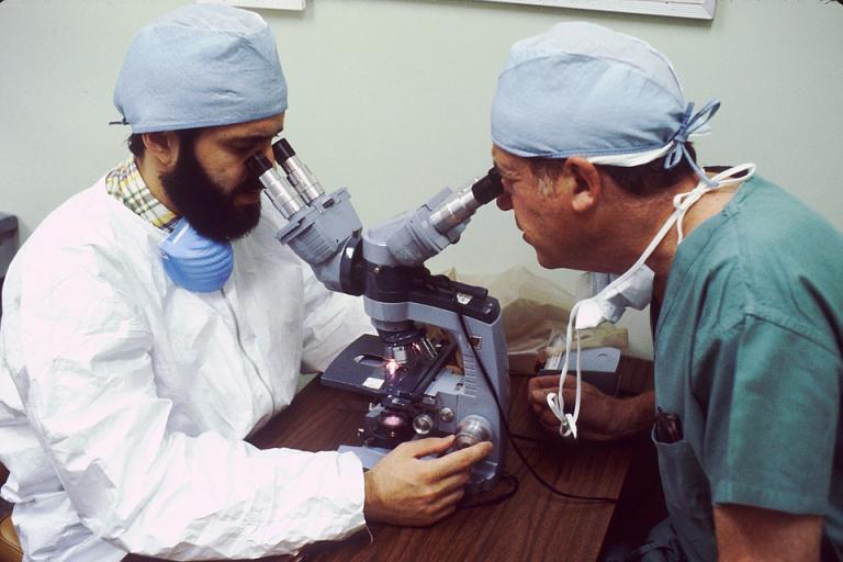 A picture of two man looking into a microscope. 